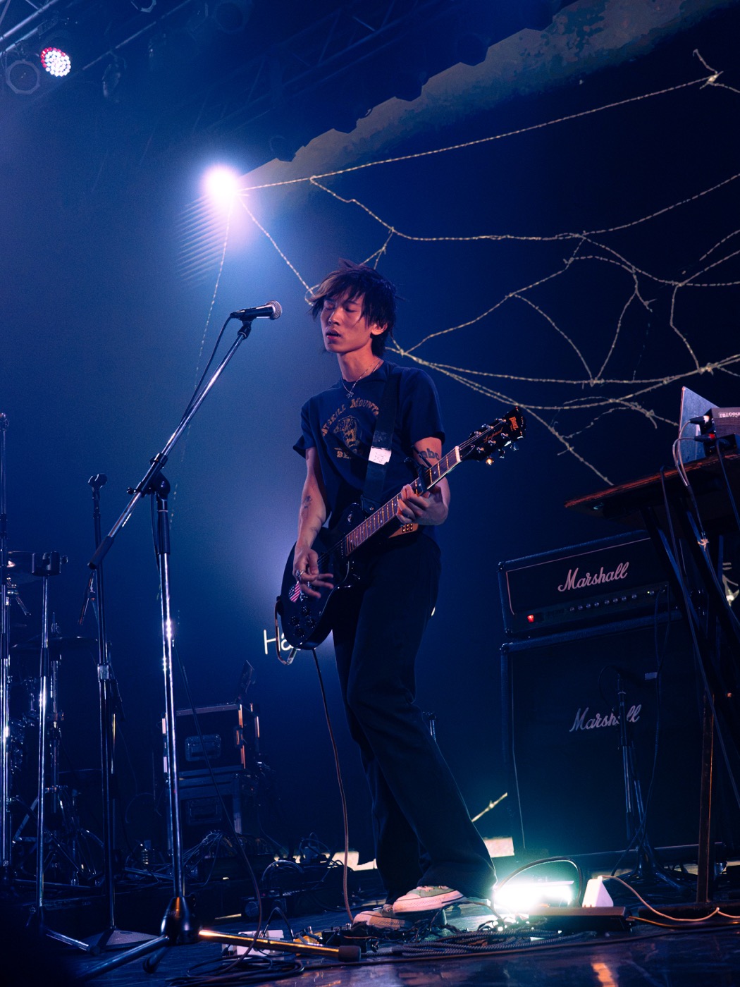 Harry Teardrop playing guitar beneath blue stage lighting