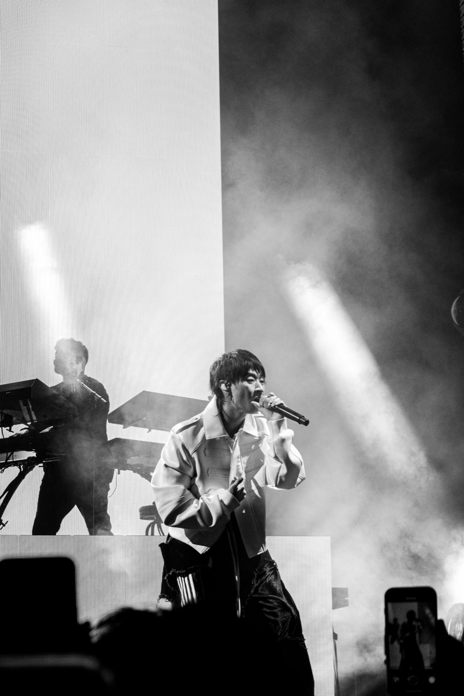 Black-and-white photograph of Keshi singing in a white jacket